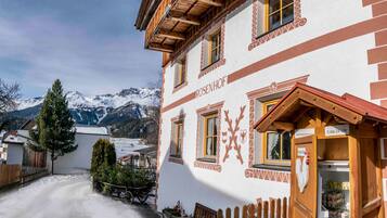 Ein traditionelles Gebäude mit Holzfassade, einem Schild für den 24-Stunden-Service und einem Blick auf schneebedeckte Berge im Hintergrund.