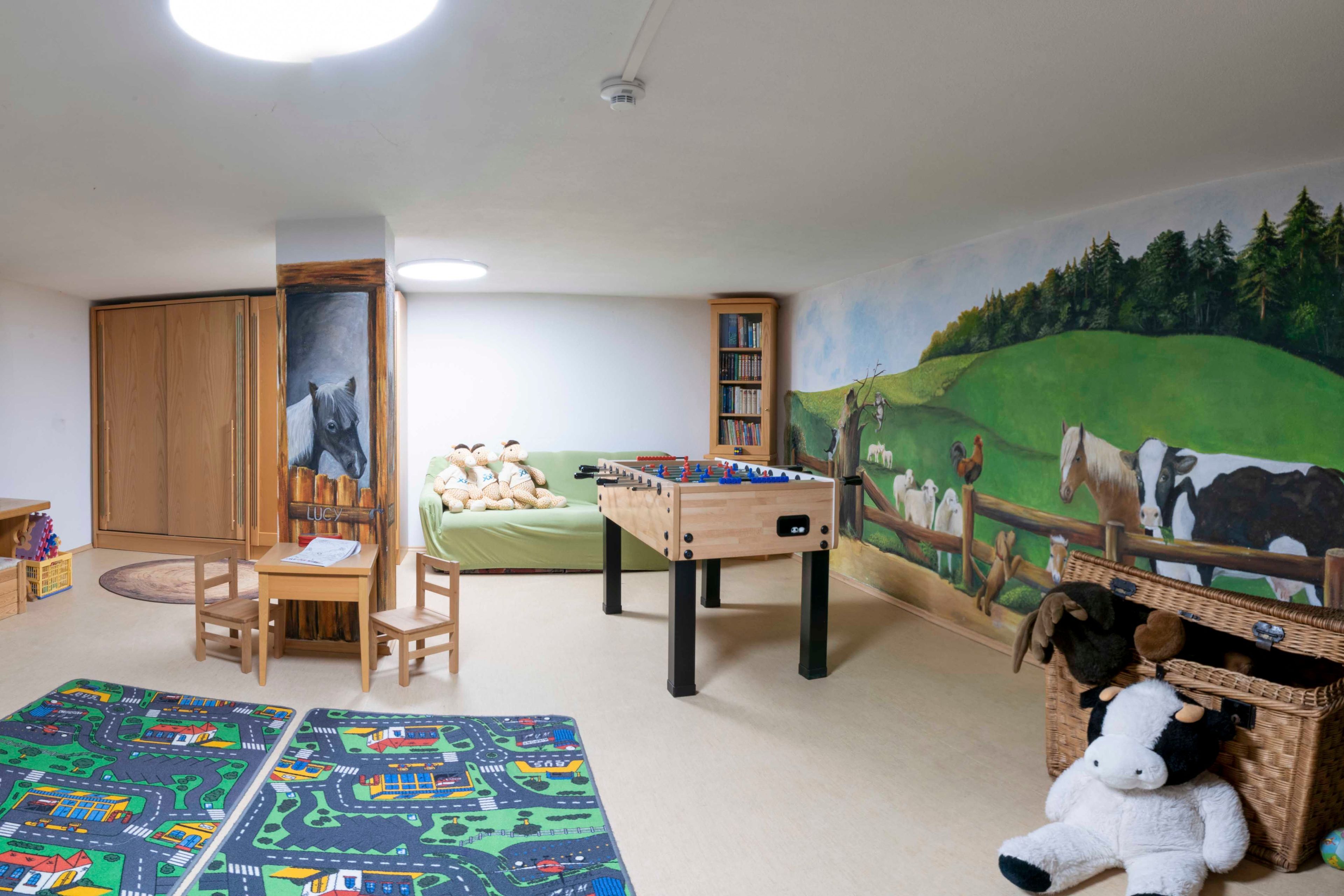 A children's playroom with a foosball table, a sofa, a bookshelf, and a mural.