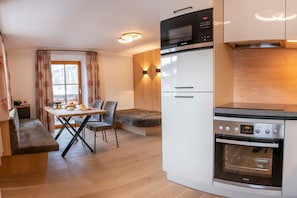 A compact kitchen with a microwave, oven, and a dining area with a bench and chairs.