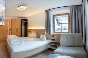 Una habitación de hotel moderna con una cama curvada, una zona de estar, un ventanal con cortinas y un armario de madera.