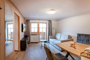 A modern living room with a wooden floor, a sofa, a dining table, and a TV mounted on the wall.
