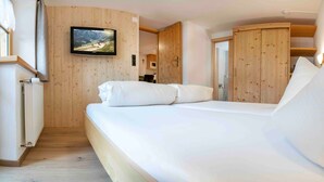 Une chambre avec un mur en bois, un lit avec une literie blanche, un téléviseur fixé au mur et une armoire.