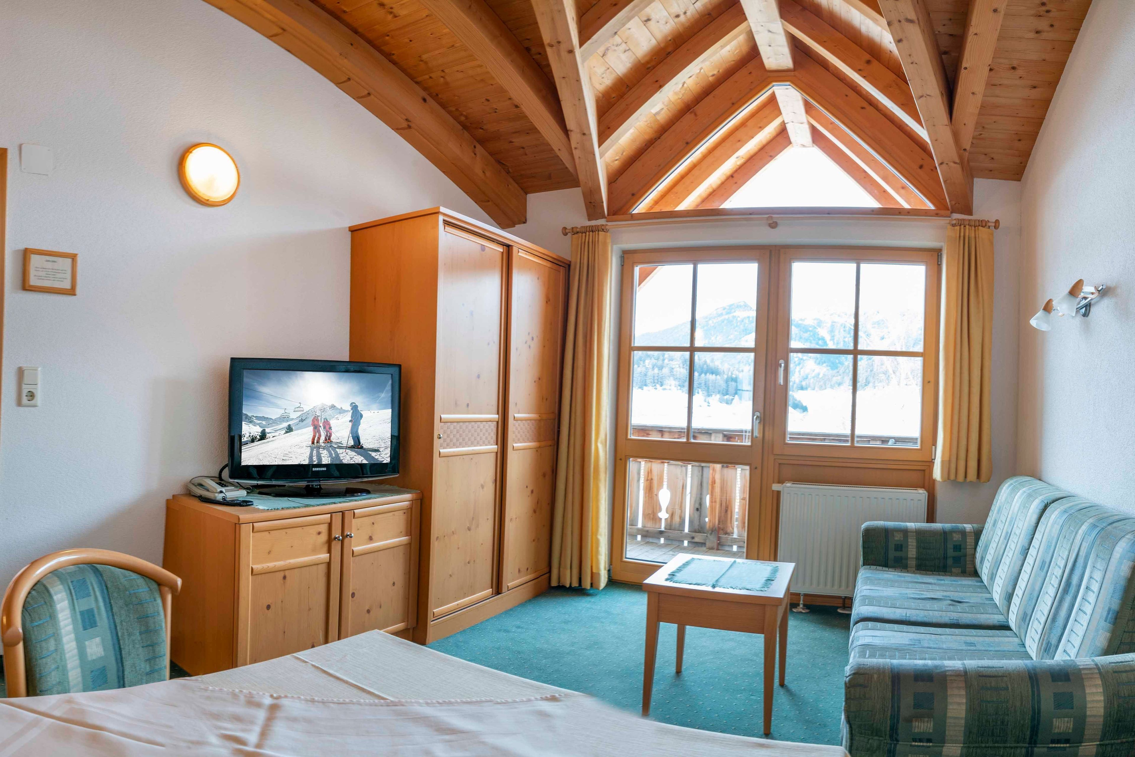 Une chambre avec un lit, une télévision, une armoire en bois, un canapé et une fenêtre donnant sur les montagnes.