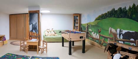 Sala de juegos infantiles con una mesa de fútbol de mesa, un sofá, una estantería y un mural.