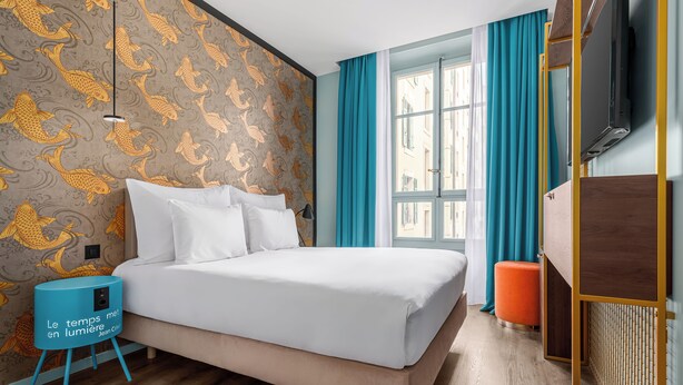 A modern hotel room with a large bed, a small stool, a TV, and a window with curtains. - Marmont Hotel (Geneva)