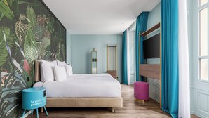 Un dormitorio con cama, una mesita de noche azul, un ventanal con cortinas y un mural en la pared.