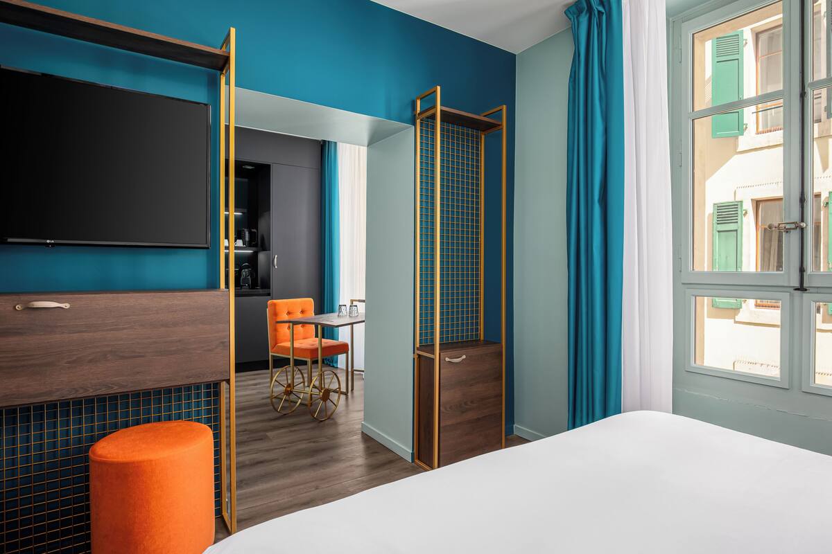 Habitación de hotel con cama, televisión, escritorio y silla, y ventana con cortinas.