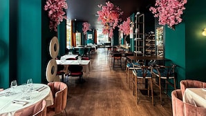 Un restaurante con paredes color turquesa, suelo de madera, sillas rosas y decoración floral en tonos rosados.