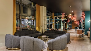 Un espacio lounge moderno con sofás tapizados en gris, una mesa de centro de cristal y una estantería azul verdoso con adornos rosados.