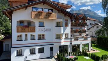 Ein mehrstöckiges Hotel mit Balkonen, einem Garten und Blick auf die Berge.