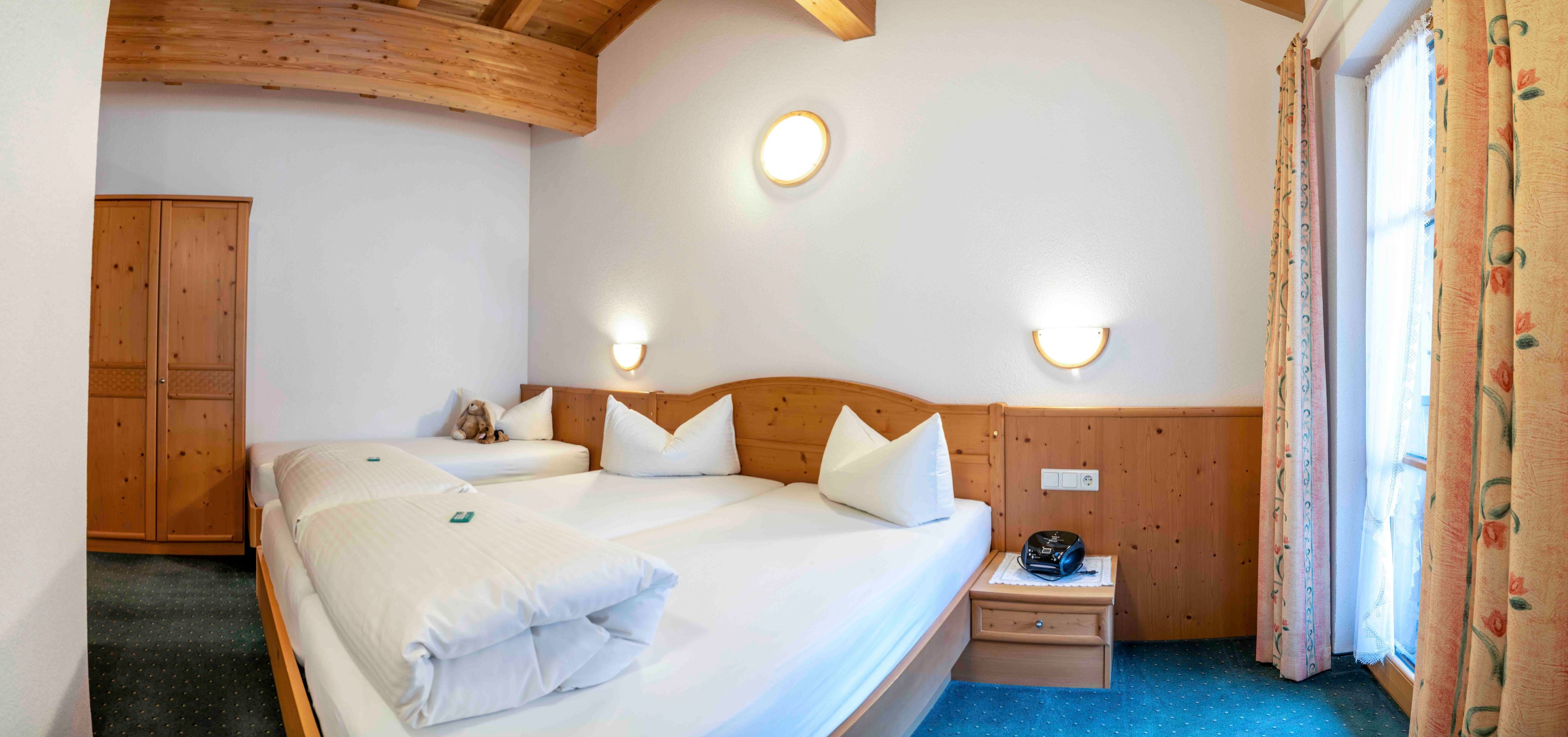 Une chambre d’hôtel avec deux lits, des têtes de lit en bois, des lampes fixées au mur, une petite table de chevet avec une radio et une armoire.