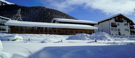 Un edificio cubierto de nieve con fachada de madera, telón de fondo montañoso y cielo despejado.