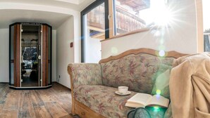 Um quarto com piso de madeira, um sofá floral, um livro e uma xícara sobre o sofá.