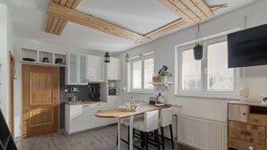 A modern kitchen with white cabinets, a wooden dining table, and a black hanging plant. - Rooms and Apartments in Eagle's Nest (Ljubljana)