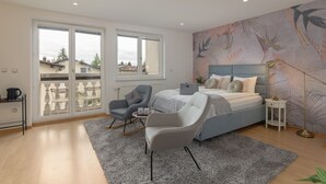 A bedroom with a bed, two chairs, a small table, and a large window. - Rooms and Apartments in Eagle's Nest (Ljubljana)