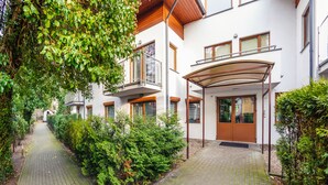 A modern residential building with a covered outdoor area, a paved pathway, and lush greenery. - Apartamenty Sun & Snow Willa Jazgór (Wladyslawowo)