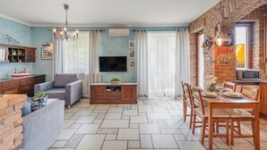 A living room with a sofa, TV, dining table, and kitchen area with a brick wall and a microwave. - Apartamenty Sun & Snow Willa Jazgór (Wladyslawowo)