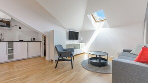 A modern apartment with a kitchen, dining area, and living room. It features a skylight, a flat-screen TV, and a grey sofa with a red pillow. - Apartamenty Sun & Snow Willa Jazgór (Wladyslawowo)