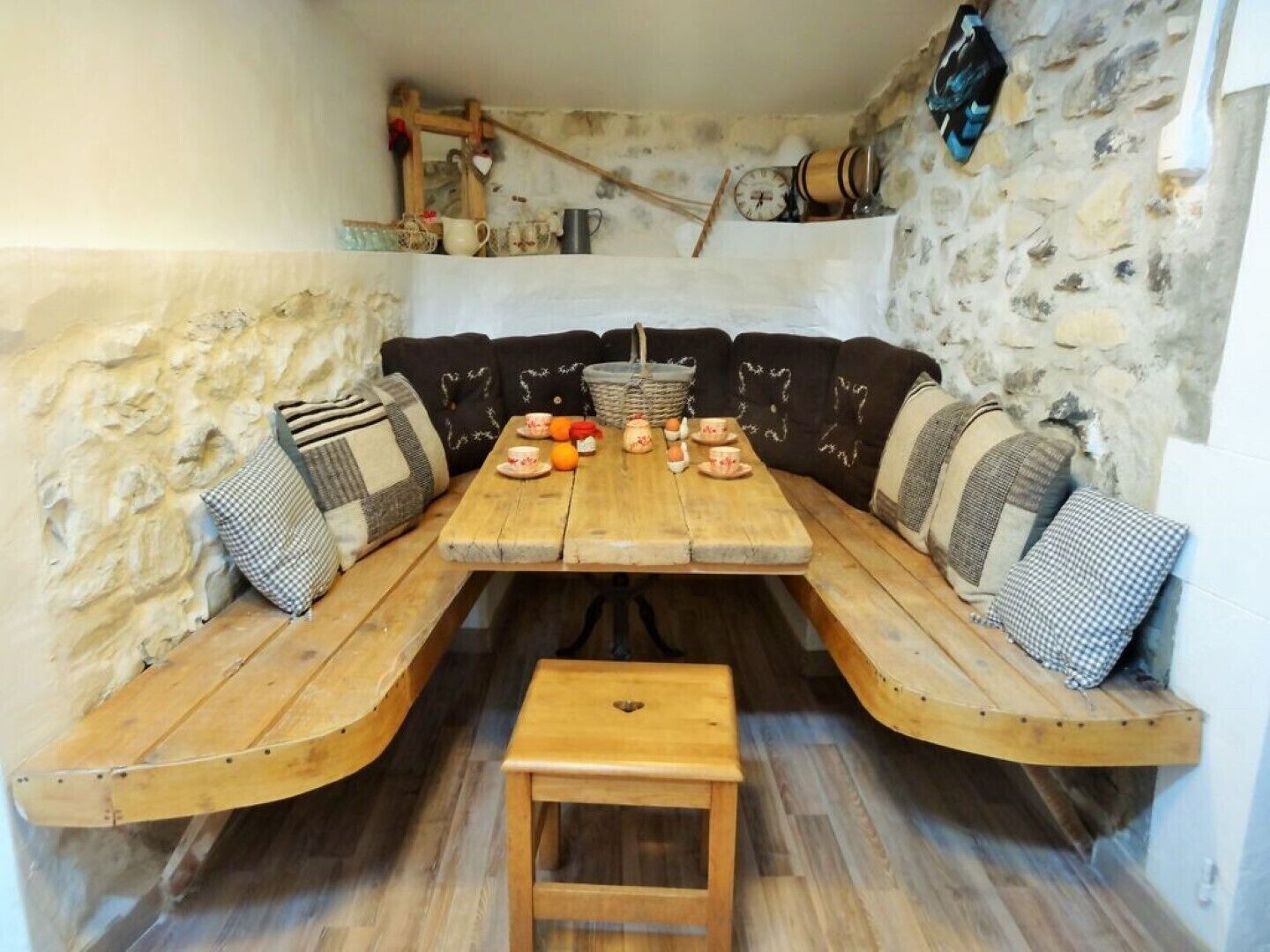 A rustic dining area with a wooden table and bench seating, stone walls, and a small stool.