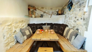 Un coin repas rustique avec une table et des bancs en bois, des murs en pierre et un petit tabouret.