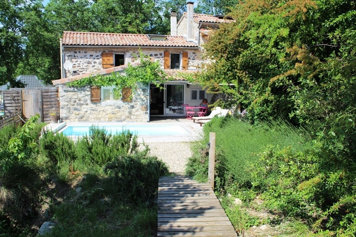 Una casa de piedra con piscina, terraza de madera y jardín.