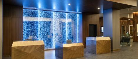 A reception area with a modern design, featuring a blue illuminated wall and two wooden reception desks.