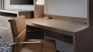 A hotel room with a wooden desk, a brown leather chair, a gold lamp, and a flat-screen TV.