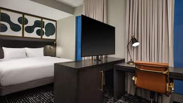Una habitación de hotel con cama, escritorio con televisor, silla y lámpara.