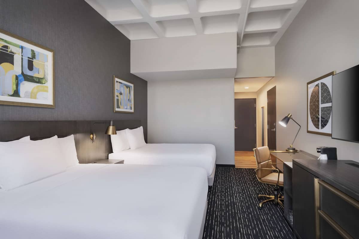 A hotel room with two beds, a desk, a chair, and artwork on the walls.