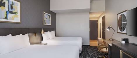 Habitación de hotel con dos camas, un escritorio, una silla y obras de arte en las paredes.