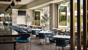 Ein modernes Restaurant mit einer langen Theke, blauen Stühlen und großen Fenstern, die einen Blick ins Freie ermöglichen.