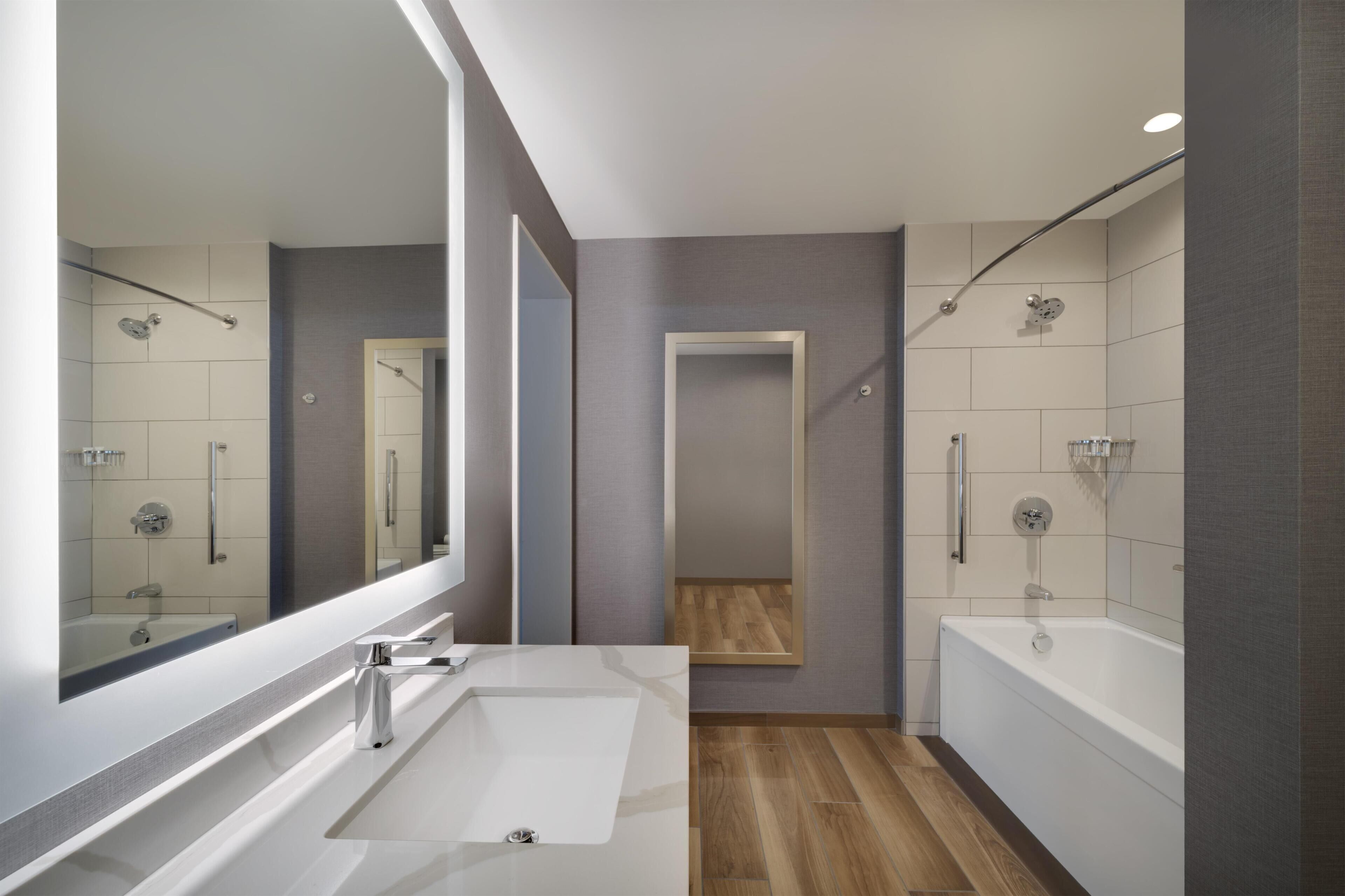 Un baño moderno con un espejo grande, una bañera y una zona de ducha.