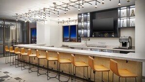 A modern kitchen with a long bar area, bar stools, a flat-screen TV, and a coffee machine. - Hyatt House LAX/Century Blvd (Los Angeles)