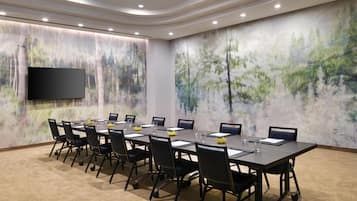 A conference room with a long table, chairs, a flat-screen TV, and abstract wall art.