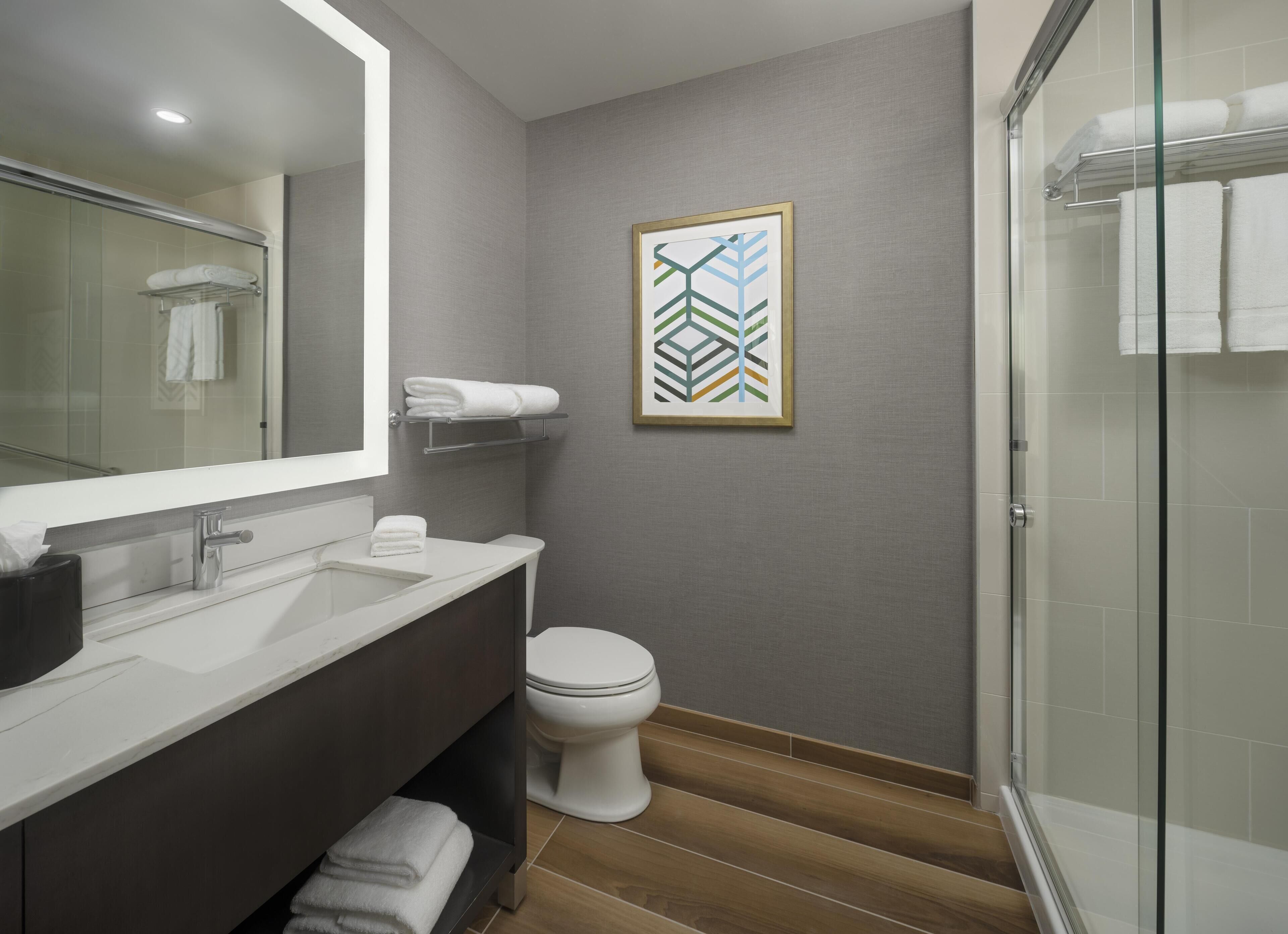 A modern bathroom with a large mirror, a white sink, a toilet, and a glass shower enclosure.
