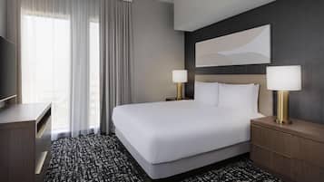 Een hotelkamer met een groot bed, twee bedlampen, een flatscreen televisie, een bureau en een groot raam met gordijnen.