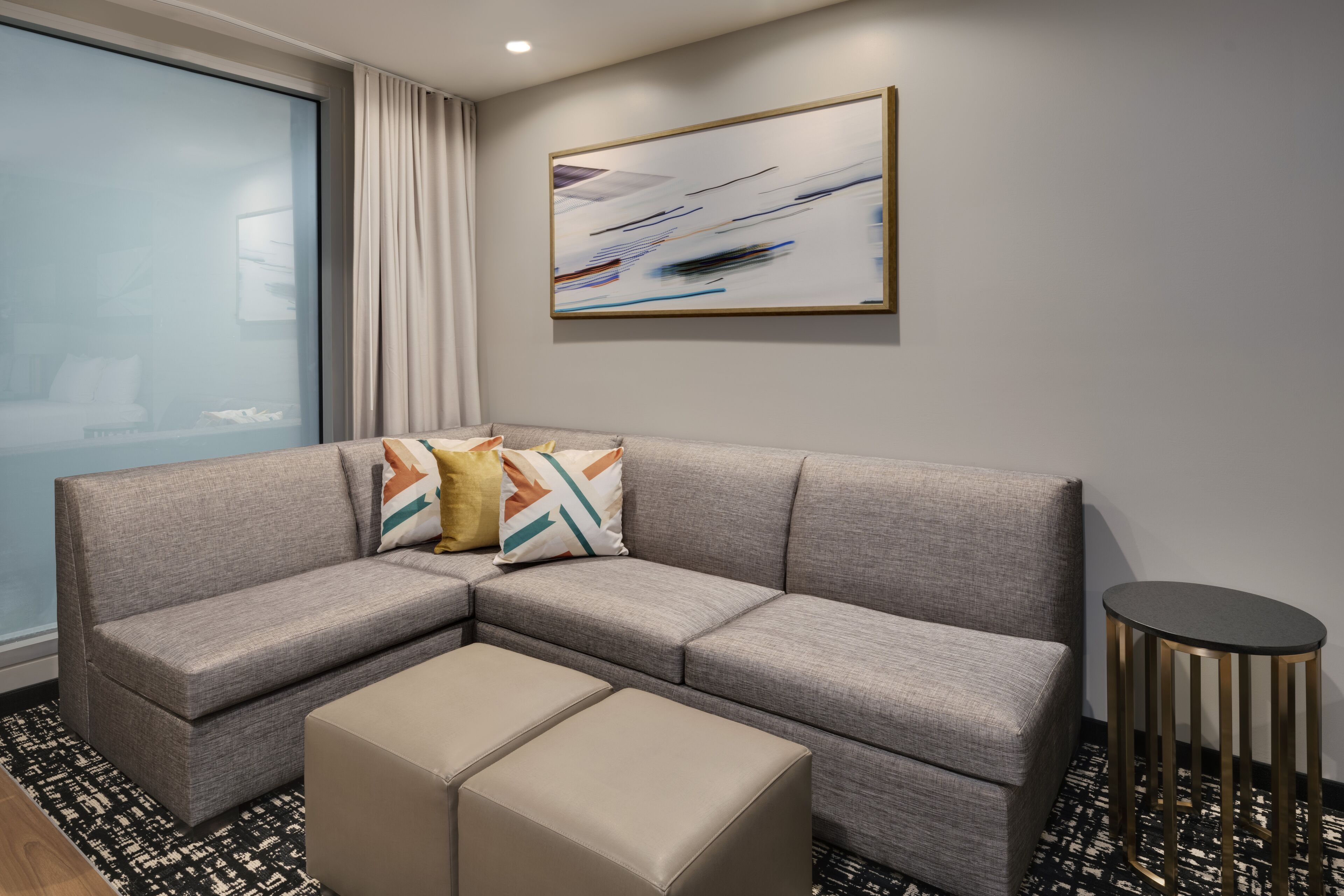 A modern living room with a grey sectional sofa, a small round table, and a large abstract painting on the wall.