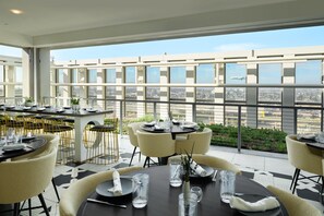 A restaurant with tables set for dining, large windows offering a city view, and a balcony with a railing. - Hyatt House LAX/Century Blvd (Los Angeles)