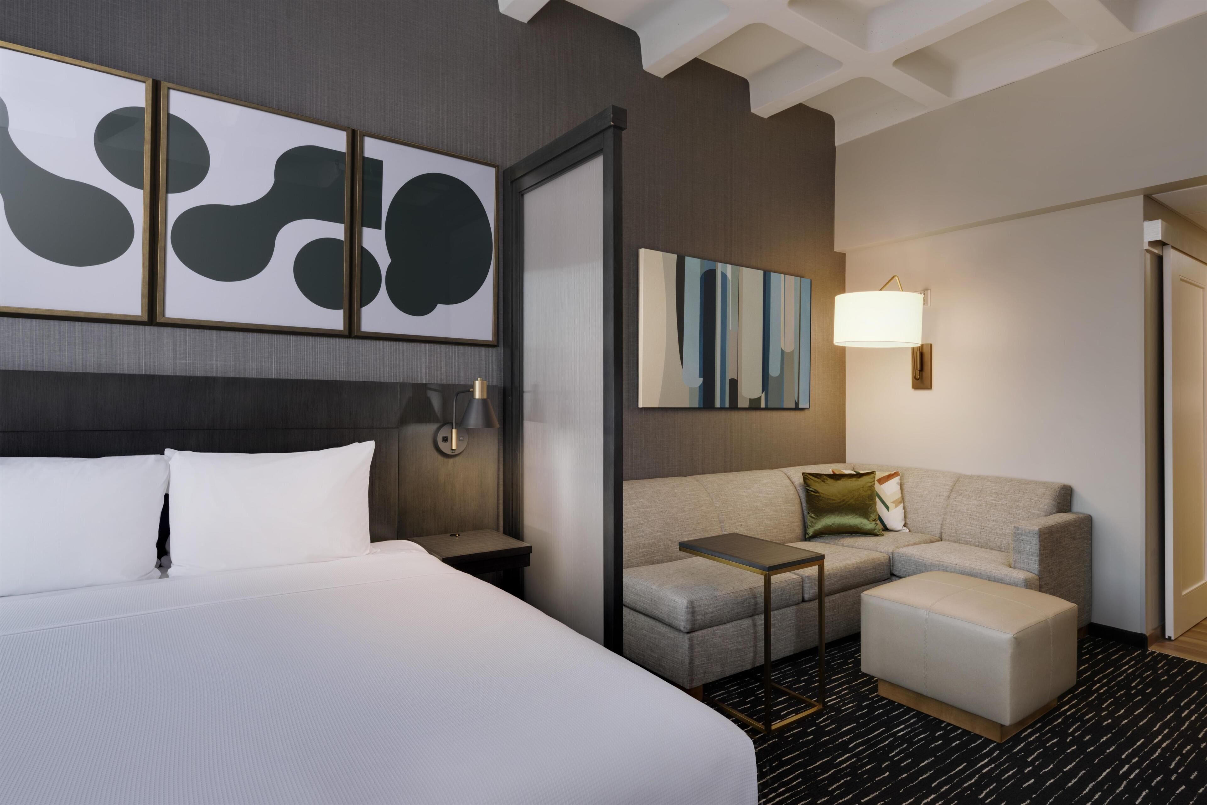 A hotel room with a large bed, a sofa, a small table, and a lamp.