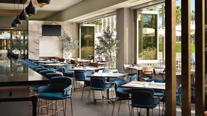 A restaurant with a bar area, multiple tables and chairs, large windows, and a stone wall. - Hyatt House LAX/Century Blvd (Los Angeles)