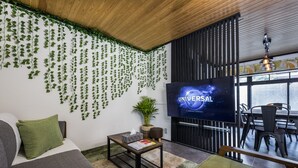 Un soggiorno moderno con un'ampia televisione a schermo piatto che mostra "UNIVERSAL", un divano, un tavolino da caffè e un'area pranzo con sedie.