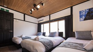 Una camera d'albergo con tre letti, soffitto in legno, ampie finestre e un quadro appeso al muro.