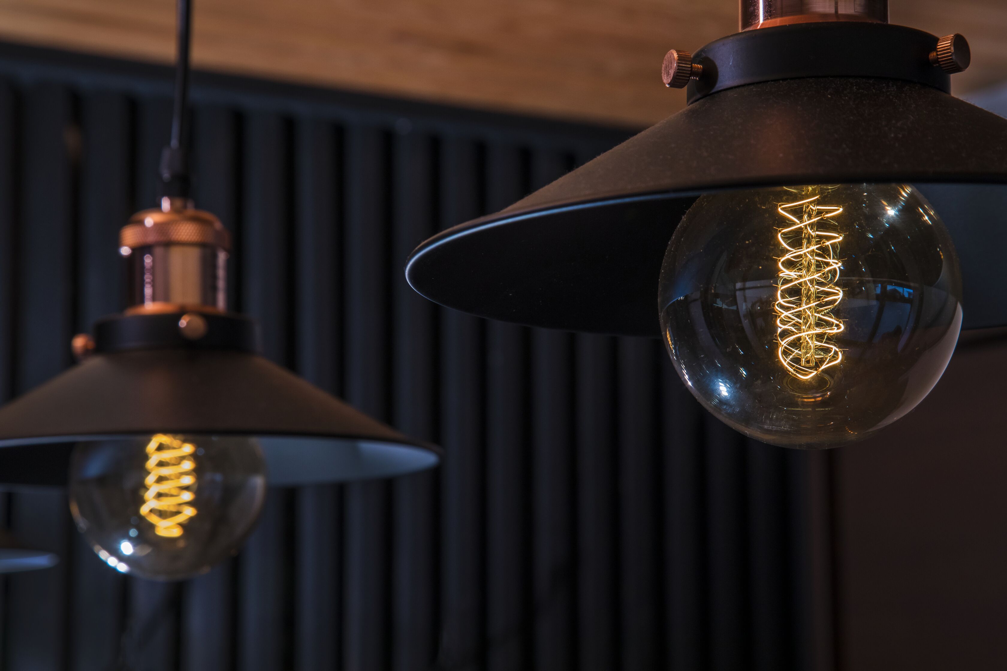 Two pendant lights with exposed filament bulbs against a dark background.