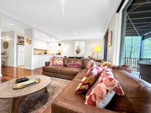 A modern living room with a brown leather sofa, a round coffee table, and a kitchen in the background.