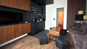 Une cuisine moderne avec des meubles de couleur sombre, un téléviseur à écran plat et un coin repas comprenant une table en bois et des poufs noirs.
