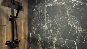 Une salle de bain avec un mur en marbre noir, un panneau en bois et une douche équipée d’un pommeau de douche à main.