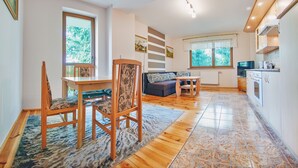 A modern kitchen with wooden cabinets, a dining area with a table and chairs, and a living area with a sofa and a TV. - Apartamenty Sun & Snow Moniuszki (Karpacz)