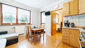 A modern kitchen with wooden cabinets, a dining table with chairs, a coffee machine, and a view of the outside through large windows. - Apartamenty Sun & Snow Moniuszki (Karpacz)