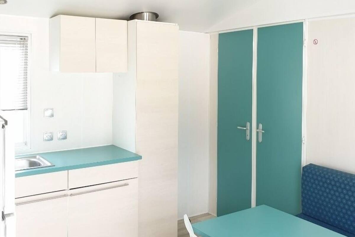 Een kleine keuken met een spoelbak, kastjes en een blauwgroene eettafel.