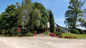 A rural house with a gravel driveway, surrounded by lush greenery and flowering plants. - Au Tour De L'Aveyron (L'Hospitalet-du-Larzac)